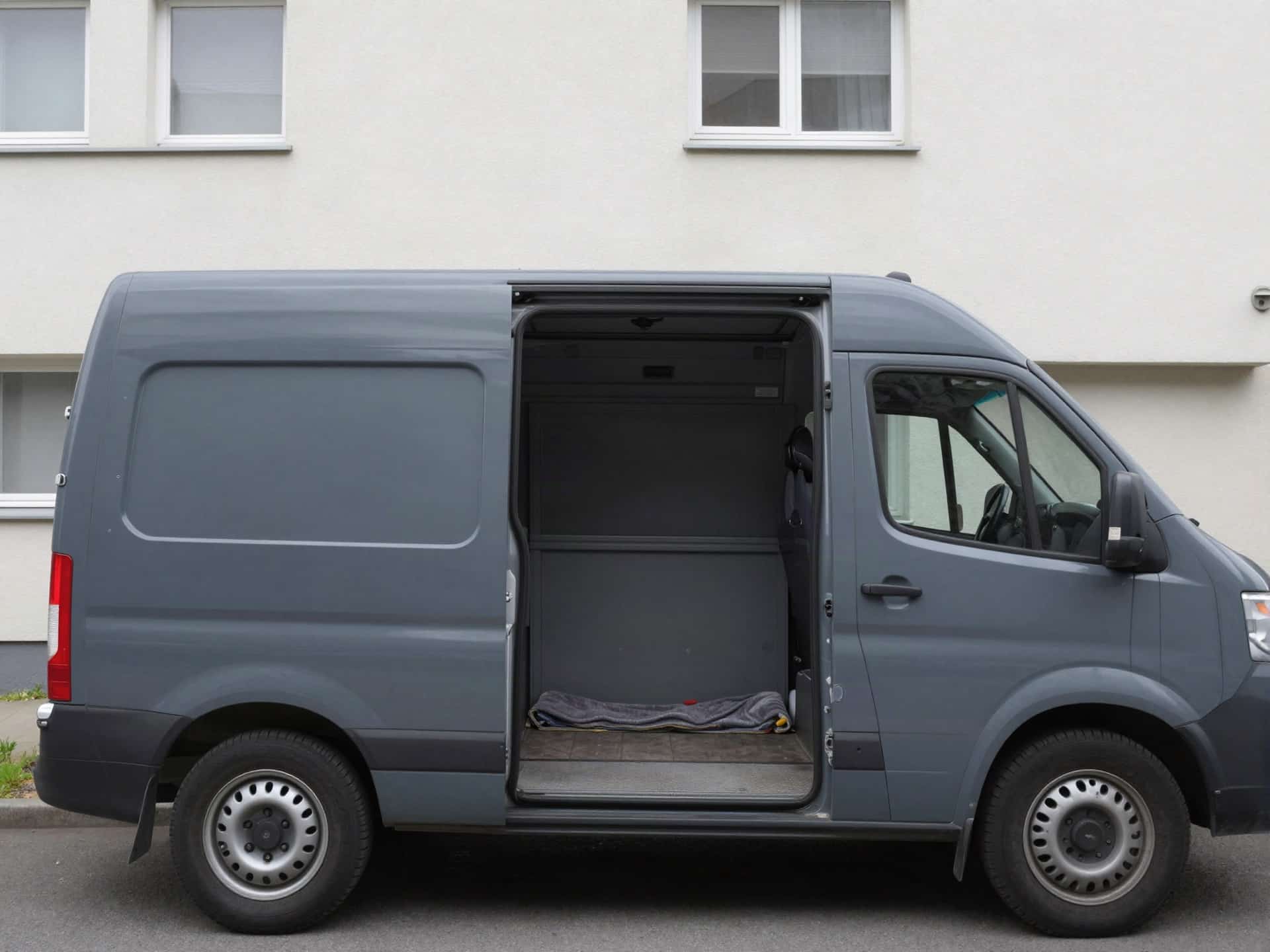 Transporter mit geöffneten Hecktüren und leerer Ladefläche vor einem Mehrfamilienhaus