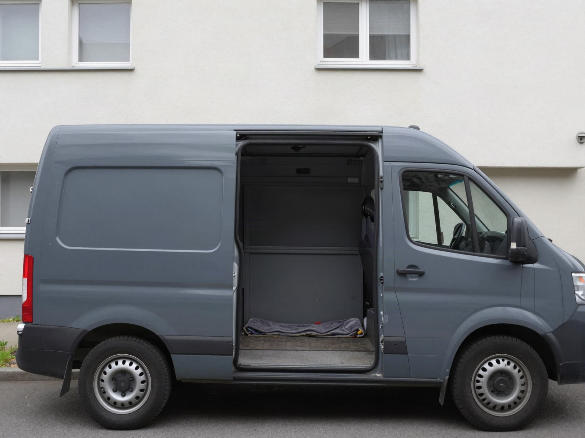 Transporter mit geöffneten Hecktüren und leerer Ladefläche vor einem Mehrfamilienhaus